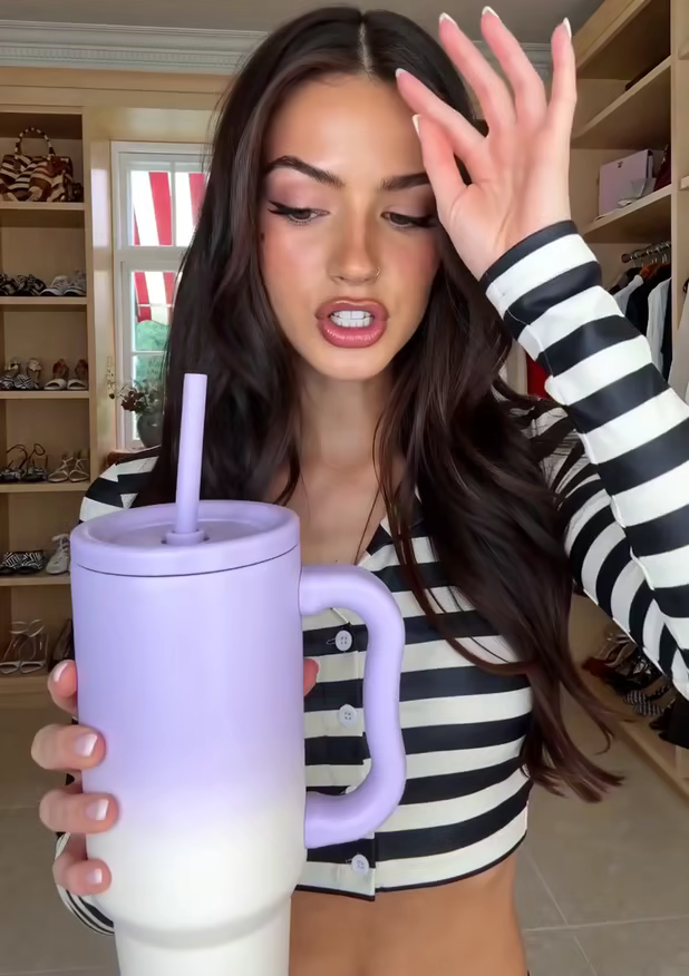 A creator running a hand through long dark hair, lilac tumbler in the other hand
